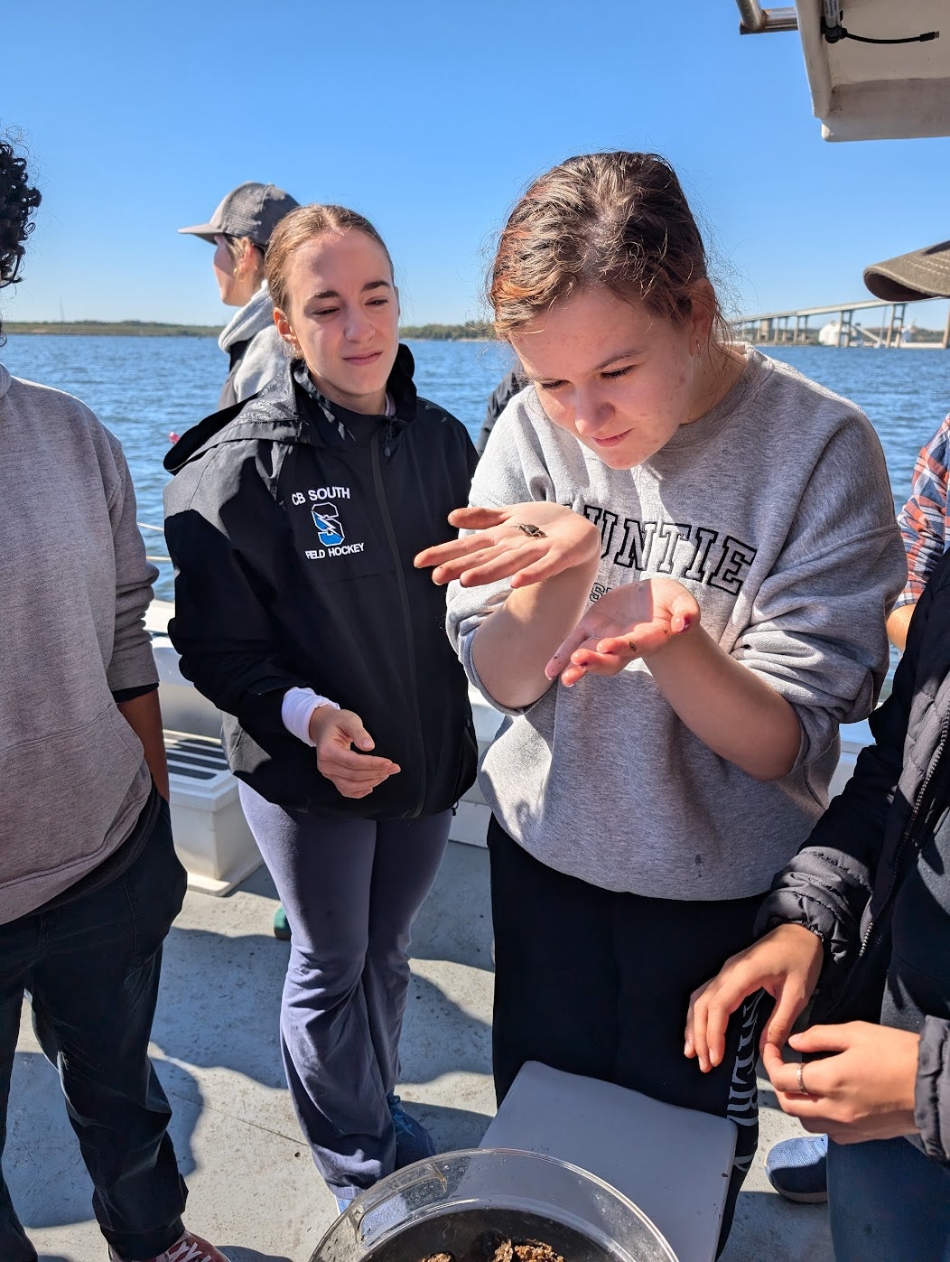 Students on boat surrounded by blue water look closely at a small crab in their hand