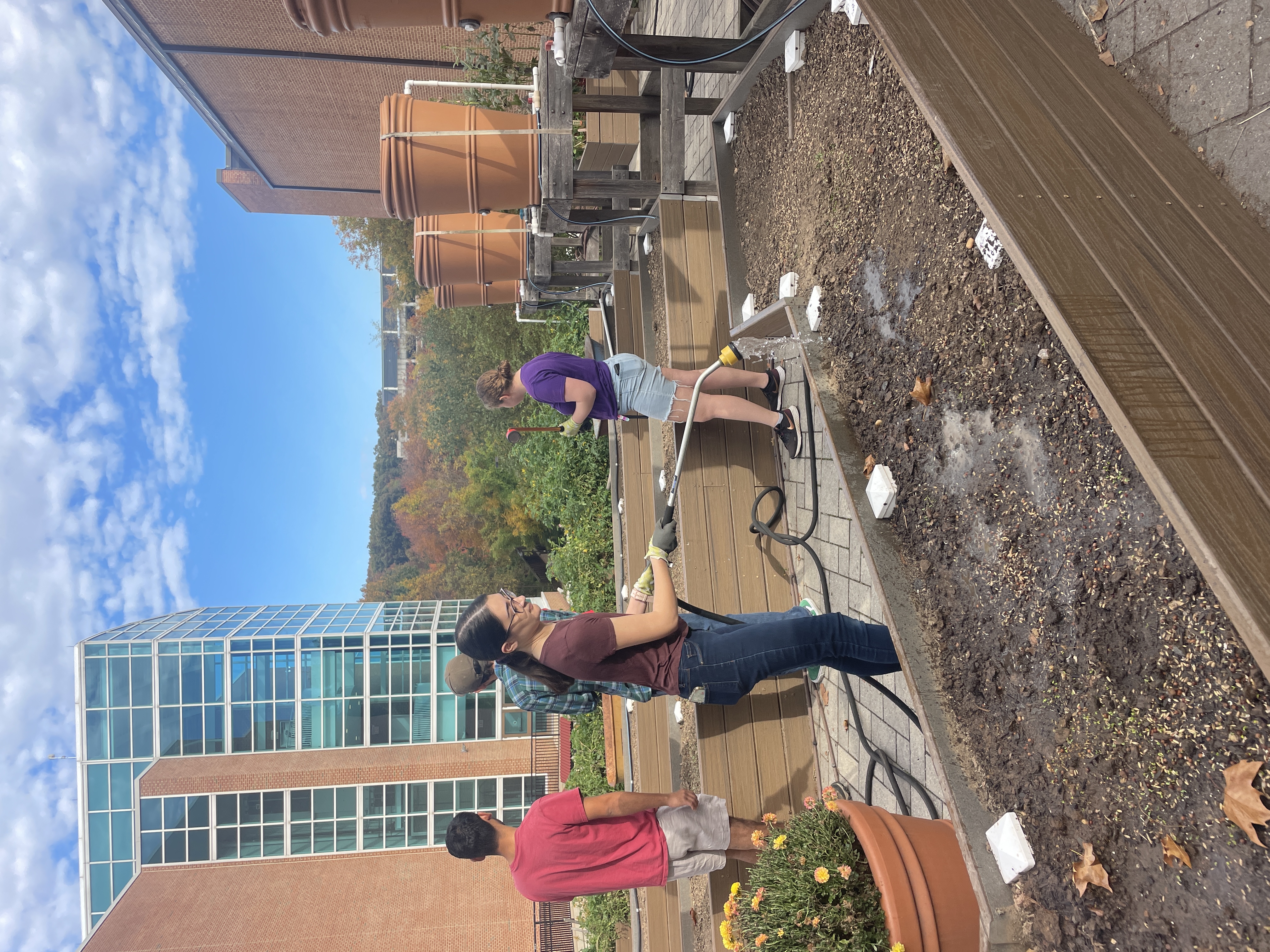 Student watering raised bed in community learning garden while others lay out seeds