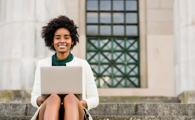 Student with laptop sitting on steps of academic building