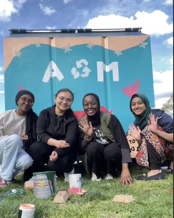 Students pose in front of partially painted dumpster.