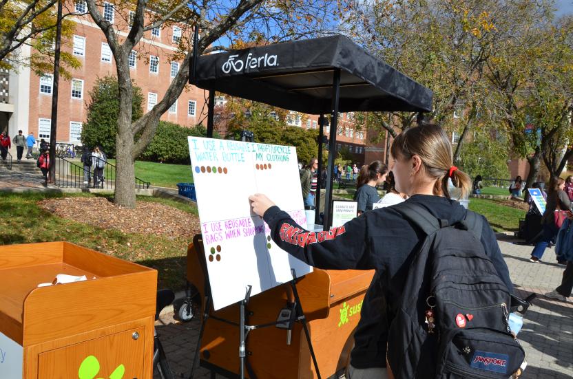 Student placing a sticker on a board that highlights sustainable actions like carrying a reusable bag and thrifting.