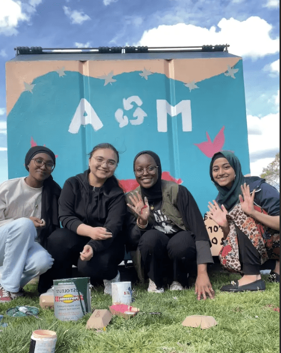 Students pose in front of partially painted dumpster.