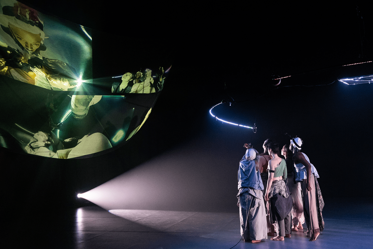 Dancers stand next to a projected image of a darkened planet