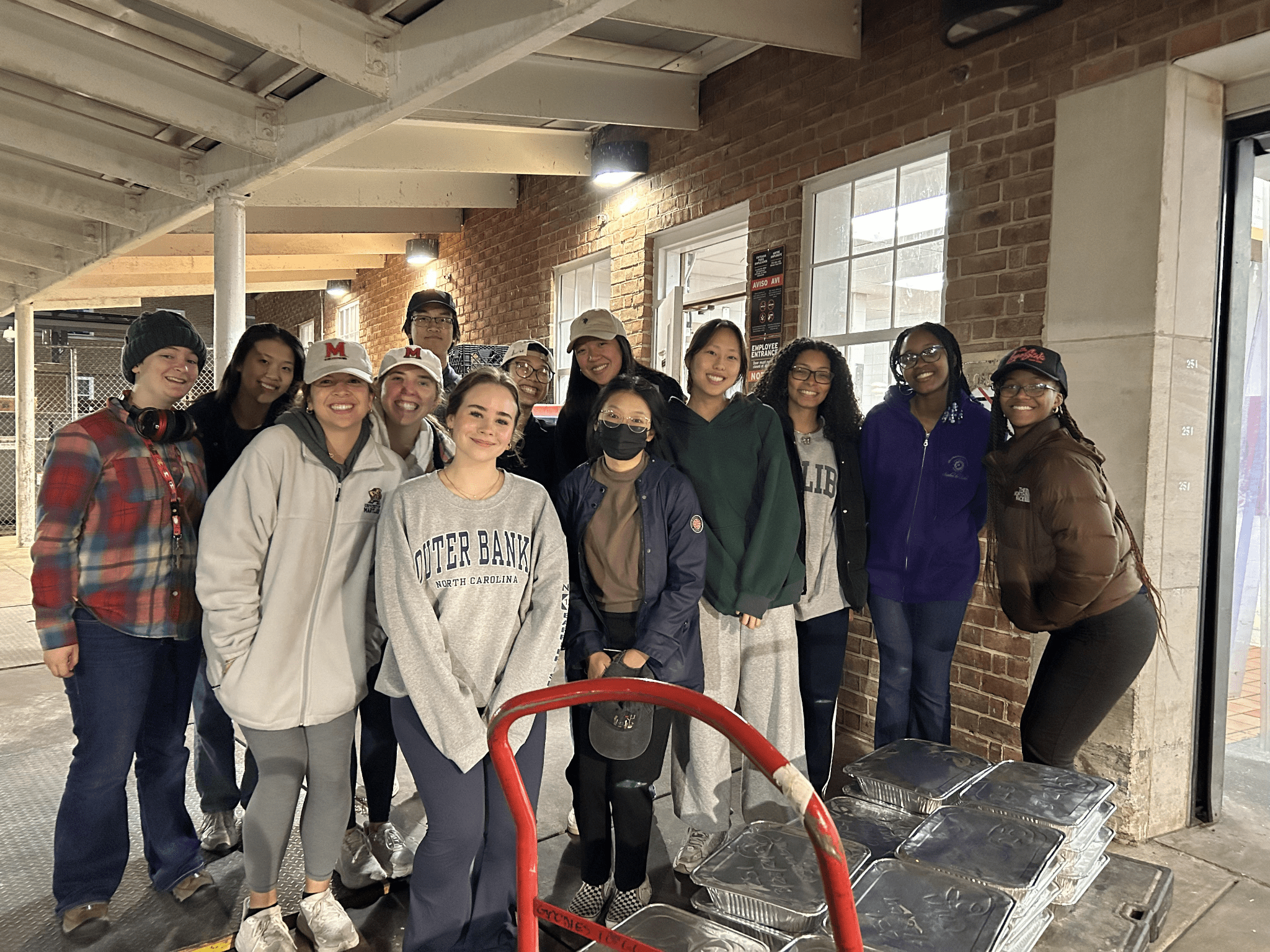 Student members of the Food Recovery Network stand outside of a campus dining hall with a cartful of recovered food.