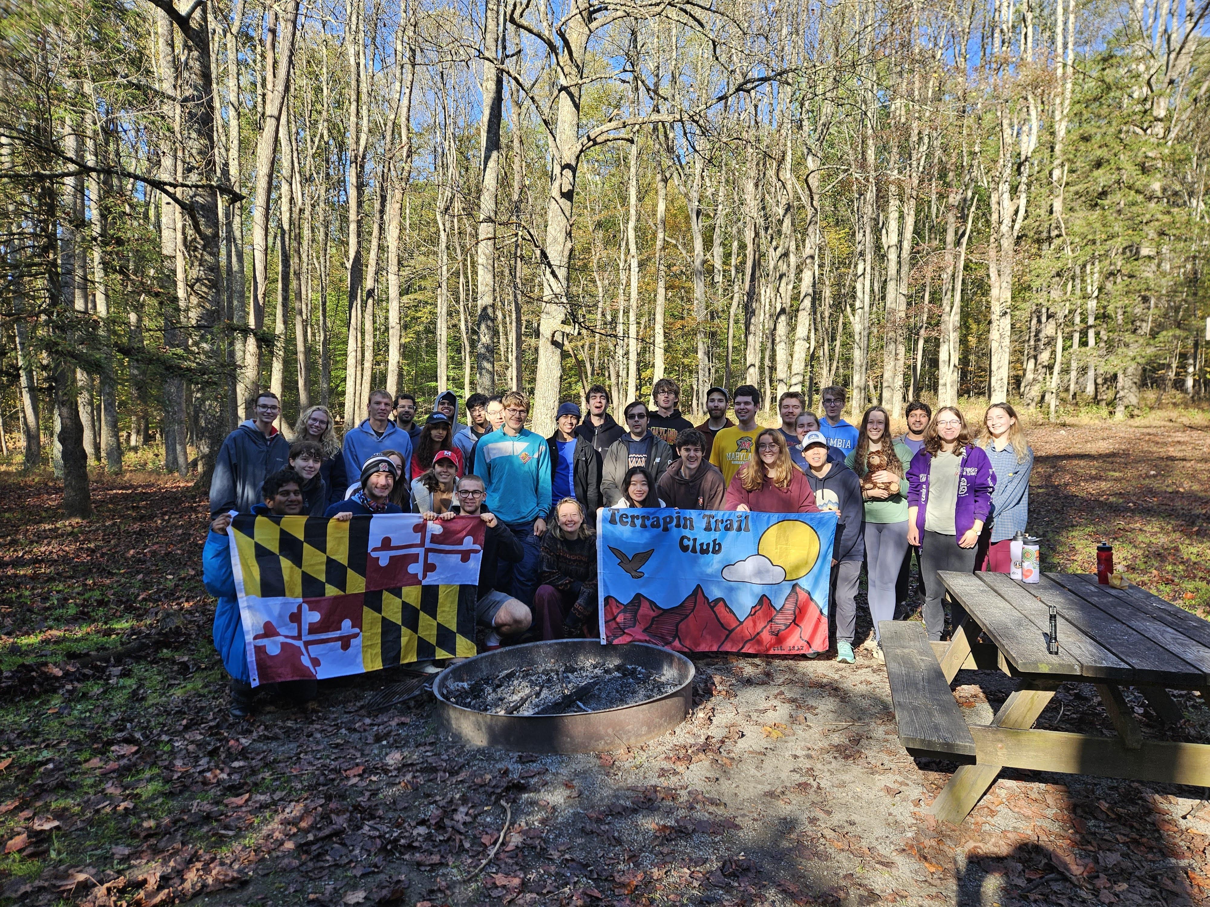 Students posing in a forest hold up the Maryland flag and a Terrapin Trail Club flag.