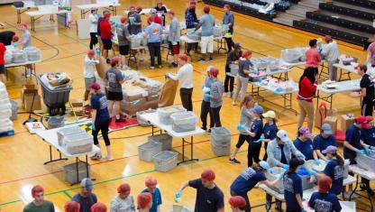 Students and community members exploring tables and exhibits at an indoor event in a gymnasium.