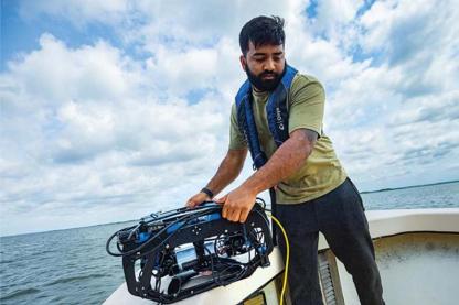 Researcher on a boat lowering scientific equipment into the water for field research.