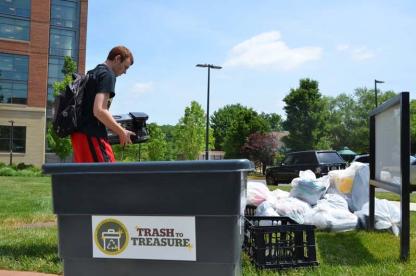 Student sorting bags of waste into a campus recycling and trash collection container.
